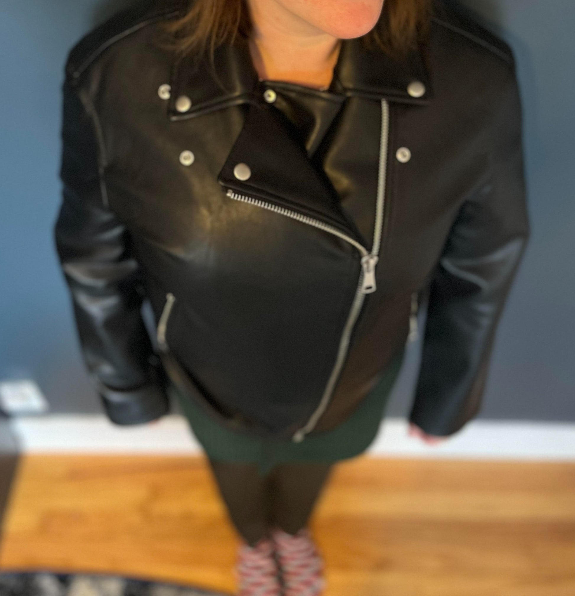 Woman wearing black vegan leather motorcycle jacket, standing against blue wall